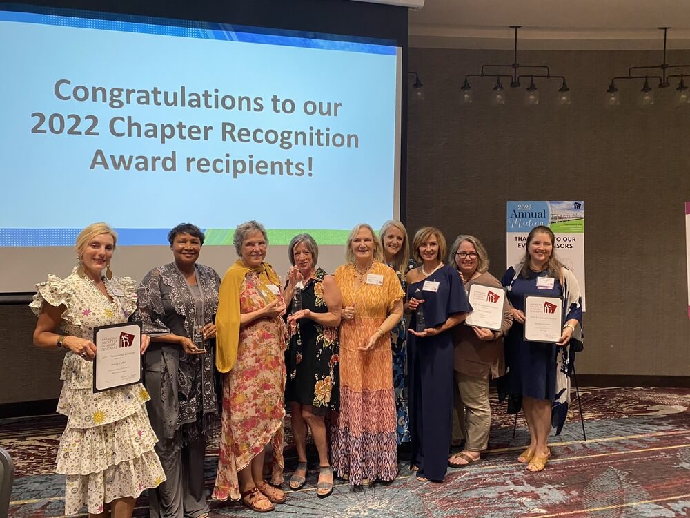 9 interior designers stand in front of a screen all holding awards at the 2022 annual ASID Carolinas meeting